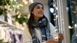 © Thares2020 - A woman wearing a beanie and scarf smiles while looking at string lights on a storefront window during evening