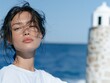 © maxbarbosac - Young european brunette woman in white shirt posing near blue sea with mediterranean architecture and sunlight Concept of peaceful lifestyle