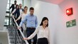 © Jafree - Group of office colleagues descending stairs during emergency evacuation. Employees walking down staircase following fire alarm and exit sign in building. Professional safety training exercise