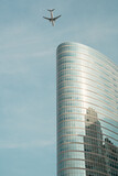 Airplane flying over a modern glass skyscraper in a city.