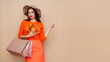 © Oleg Gekman - A beautiful young woman in an autumn fashionable outfit with shopping bags and round hat pointing aside at free space over beige background