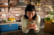 © Davor - Smiling woman using smartphone in home kitchen with fresh groceries