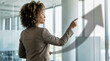 © Sergei - Businesswoman pointing at an upward trend arrow on a glass wall in a modern office. Confident professional woman showing financial growth and success