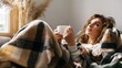 © Olya Pilipchik  - Young woman relaxing on sofa at home, enjoying warm beverage under plaid blanket, contemplating future possibilities with cozy comfort and calm thoughts