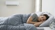 © Xenia - Young woman sleeping comfortably under cozy blanket in bedroom. Female resting in cool air conditioned room