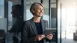 © Eve - Smiling mature businesswoman holding digital tablet in corporate office, happy senior female executive leaning on glass wall portrait, professional middle aged manager career success