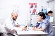 © DC Studio - Doctor explains treatment during child consultation, doctor explaining treatment to mother of sick child in hospital office holding pills bottle.