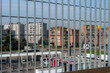 © massimo_g - Moderni edifici residenziali visti attraverso una recinzione metallica con sbarre verticali. Ambientazione urbana. Il cielo è limpido.