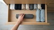 © SimpleDesignStudio - Person Organizing Rolled Clothes in Wooden Drawer Using KonMari Method for Minimalist Home Storage and Closet Organization