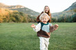 © morrowlight - Smiling little baby girl 1-2 year old running from her mother in green grass lawn and mountain landscape at background. Motherhood.