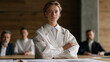 © forenna - Imposter syndrome visualized as a young Belarusian architect standing at the head of a conference table, presenting building drawings to senior colleagues, her posture slightly