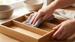 © Stitch - Hands cleaning a wooden bamboo cutlery organizer tray with a gray microfiber cloth