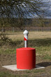 © Gerhard Paukstat - Eine rot markierte Grundwasser-Messstation steht auf einem Betonsockel in einer ruhigen ländlichen Landschaft.