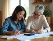 © Vadym - Two women with calculator review finances at home. Smiling elder woman and young adult happy discussing bills planning budget. Family work together on home office table.