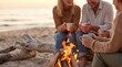 © velikiyzayats - Mature friends enjoying hot drinks by a beach bonfire at sunset, group of middle aged people relaxing outdoors, cozy autumn evening lifestyle concept