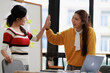 © MINAE - Successful women colleagues giving high five celebrating business goal achievement, expressing collaboration, teamwork, and success in a modern office environment