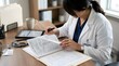 © Hossen - A female physician in a white coat reviewing patient medical documents at a wooden office desk with health care physician healthcare