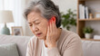 © Formoney - Elderly woman pressing ear in discomfort on living room sofa