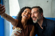 © Nenad - Portrait of a diverse romantic couple in restaurant having lunch and using a mobile phone and taking a selfie