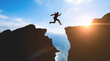 © Celt Studio - Businessman silhouette jumping across mountain gap during bright sunrise representing corporate risk extreme challenge ultimate success overcoming business obstacles achieving goals