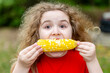 © Volodymyr - Boiled corn looks tasty and yellow. Boiled maize snack for happy childhood. Young girl eating boiled sweet cob. Outdoor food portrait shows boiled kernels.
