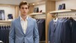© mihrzn - A confident young man in a light blue suit stands in a high-end menswear boutique surrounded by racks of tailored suits and ties.