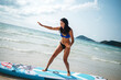© NDABCREATIVITY - Fit Asian woman posing with a stand-up paddleboard on a sunny tropical beach