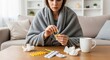 © Herlita - Sick Young Woman Wrapped in Blanket Taking Medication and Pills While Sitting on Sofa at Home During Flu Season