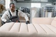 © Serhii - African american Furniture maker upholstering sofa in factory warehouse