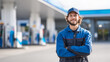 © KotBaton - Smiling gas station attendant standing confidently at a modern fuel station. Portrait of a professional service worker representing customer service, energy industry and retail business.