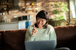 © Davor - Smiling woman on laptop video call in living room