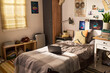 © pressmaster - Wide angle shot of student bedroom featuring laptop on bed, study desk, books, suitcase, personal decor, suggesting college living, remote learning, youth lifestyle marketing