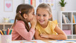 © Vyatcheslav - Young girl whispering a secret to her smiling friend at a desk. Happy children sharing secrets in a classroom. Friendship and childhood concept