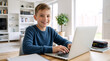 © Vyatcheslav - Happy young boy using a laptop at home. Smiling child typing on a computer for online learning and homework in a bright living room