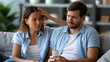 © Laura - Latin couple feeling the intense heat and seeking relief while sitting together at home on the sofa, heatwave discomfort, indoor cooling need, with copy space
