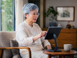 © PixelFoundry - Senior woman using a tablet on a stand at home