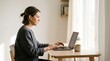 © olga_demina - A focused woman sits at a wooden table, using a laptop in a bright room. She is searching for a new career path, intent on finding a way to quit her current job and pursue new professional goals