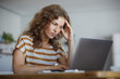 © Westend61 - Woman sitting with head in hands while working on laptop at home