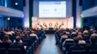 © CuteBee - Audience viewing business presentation on stage in large dark convention hall with soft blue and green accent lighting during corporate seminar event with blurred attendees in front rows