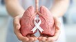 © Elena_stock - Woman holding a model of human lungs with a white ribbon for awareness. Concept of World Lung Cancer Day and respiratory health. Medical research and patient support for illness.