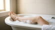 © MUHAMMAD - Close-up of smooth legs and bare feet relaxing in a warm bubble bath with white foam