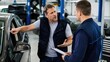 © Tati - Car owner pointing at vehicle while discussing repairs and an estimate with a mechanic in a busy auto shop workshop