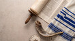 © Rhallyson - A high-angle view featuring a Torah scroll, a shofar, a tallit prayer shawl, and a kippah on a stone background, representing Jewish religious traditions.