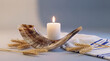 © Rhallyson - A traditional shofar horn, a lit white candle, and a striped tallit prayer shawl with wheat stalks, symbolizing Jewish holidays like Rosh Hashanah and Yom Kippur.