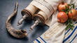 © Rhallyson - Traditional Jewish symbols for Rosh Hashanah, including a Torah scroll, a ram's horn shofar, fresh pomegranates, and a tallit on a textured dark background.