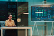 © Zamrznuti tonovi - Female it professional monitoring network security and data center performance on a large screen displaying complex dashboards
