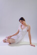 © SHOTPRIME STUDIO - Young woman in a white lace dress sits on the floor with eyes closed in a soft lit studio. Concept of beauty, fashion, elegance, and delicate style for editorial or advertising.