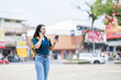 © Tj - Young Asian woman traveling and exploring an urban environment. Walking outdoors with a backpack and a cup of coffee while engaging in a phone conversation