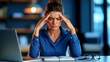 © Gasspoll - Young Female Professional Experiencing Stress While Working at Desk with Laptop and Notepad in Modern Office