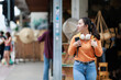 © Tj - Young Asian woman exploring exotic street market, carrying a backpack, headphones and smartphone, enjoying her travel journey and local tourism experience